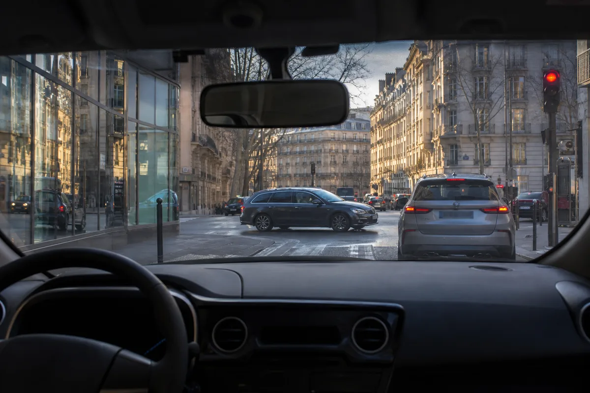 Vue depuis l&rsquo;intérieur d&rsquo;un habitacle de voiture vers un carrefour urbain à travers un pare-brise clair